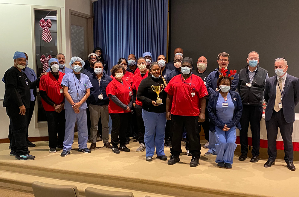 Members of the Materials Management department standing on the Zubrow Auditorium stage at Pennsylvania Hospital, with one team member holding a trophy in the center